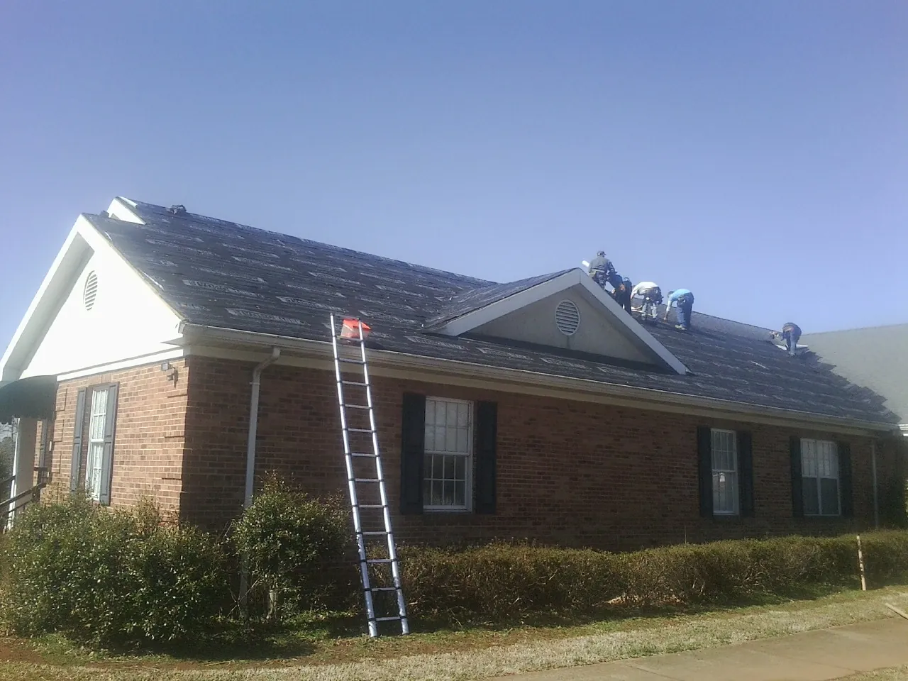 Crew tearing shingles off a brick ranch roof with a ladder set — Emergency Roof Repair work by our crew in Mathiston