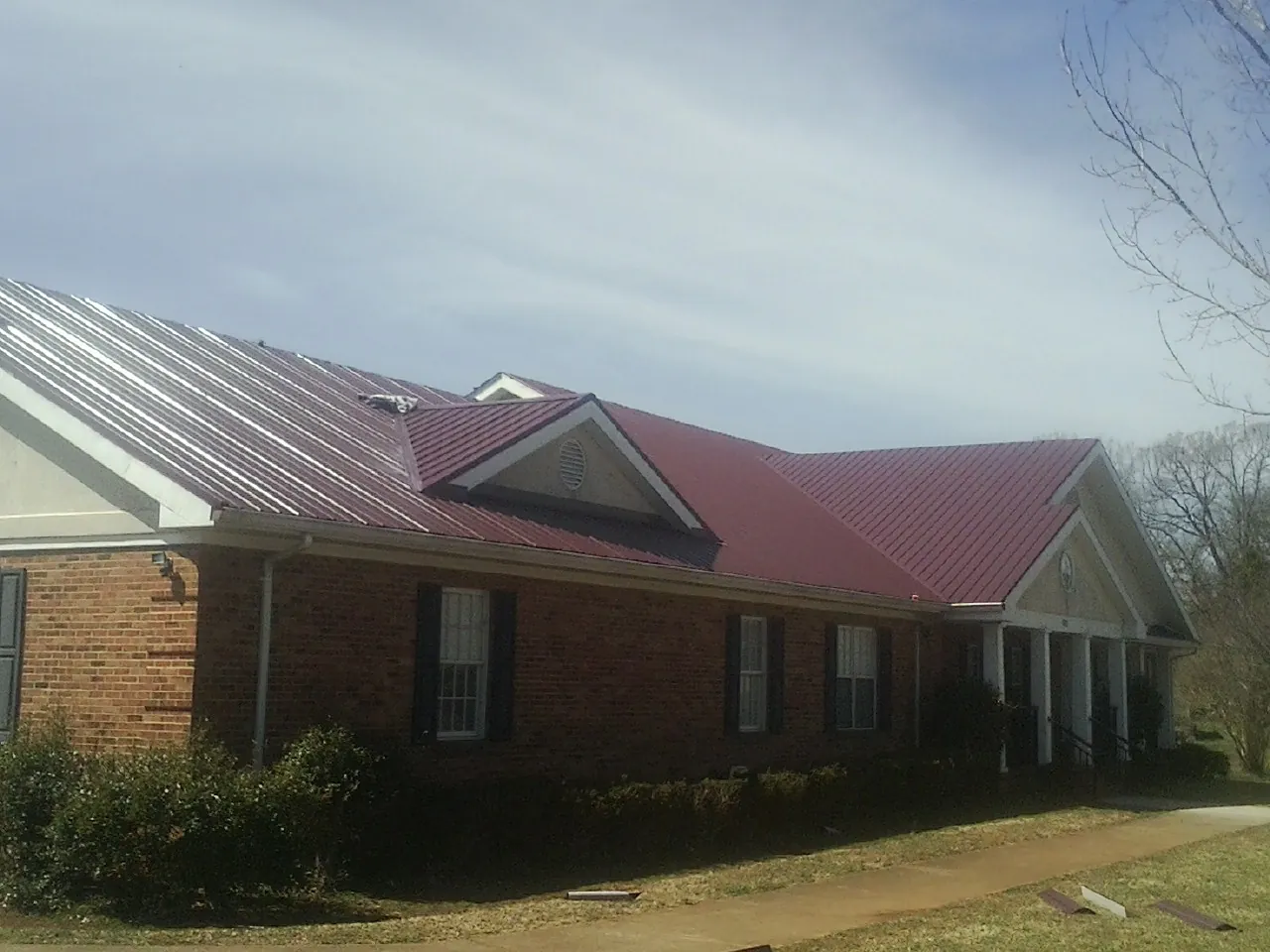 Red metal roof with gabled entries on a long brick building, from a Hail Damage Roof Repair job in Mathiston