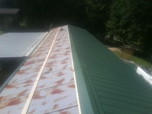 Old rusted panels beside newly installed green metal roofing — Wind Damage Roof Repair by Roofing Brothers in Mathiston