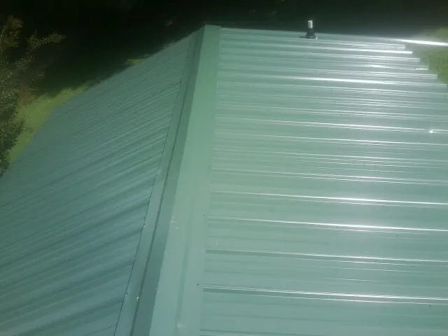 New green metal panels meeting at the ridge of a roof — Flat Roof Repair work by our crew in Mathiston