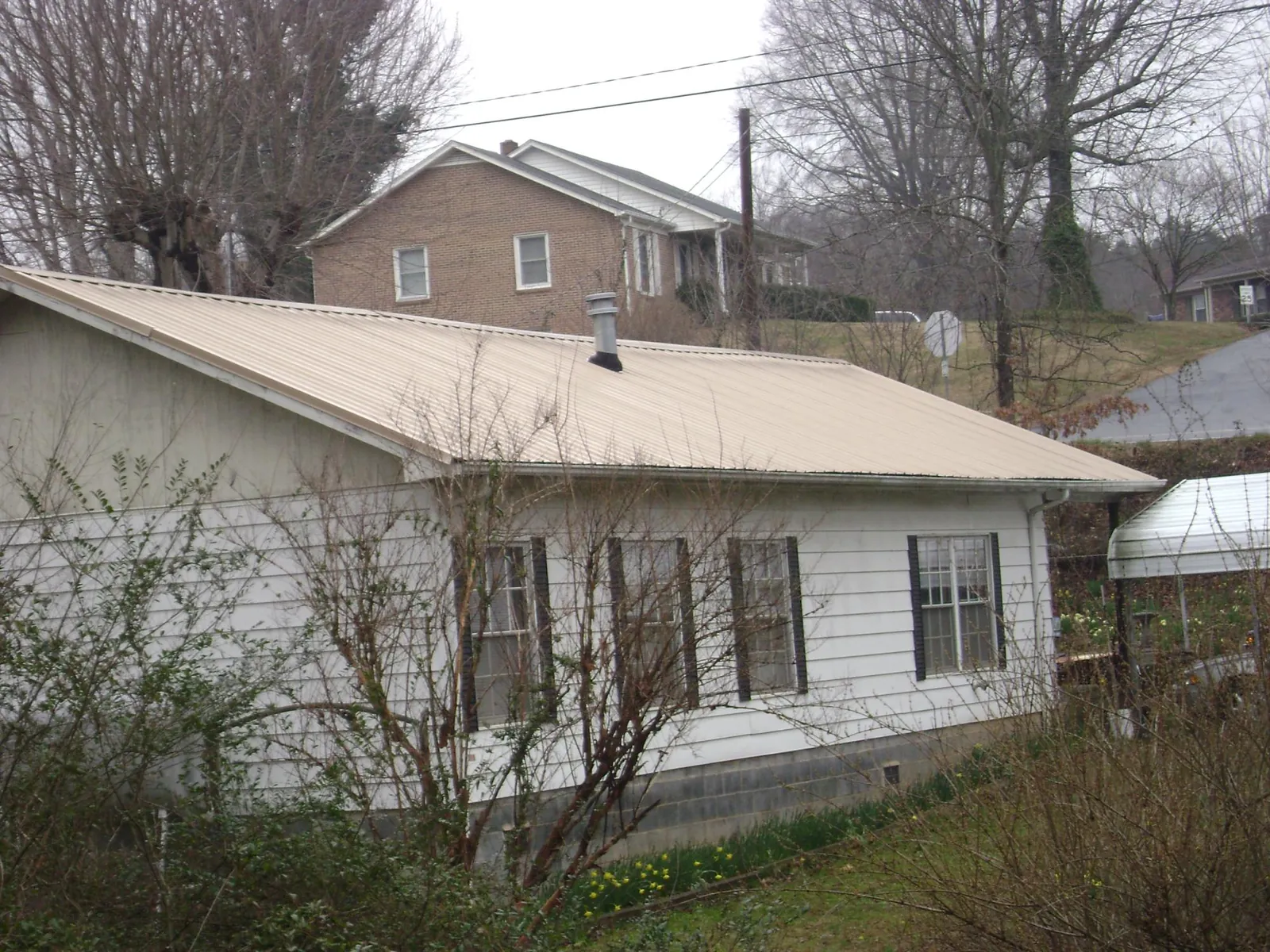 Tan metal roof on a white sided house set into a hillside — Commercial Roofing by Roofing Brothers in Mathiston