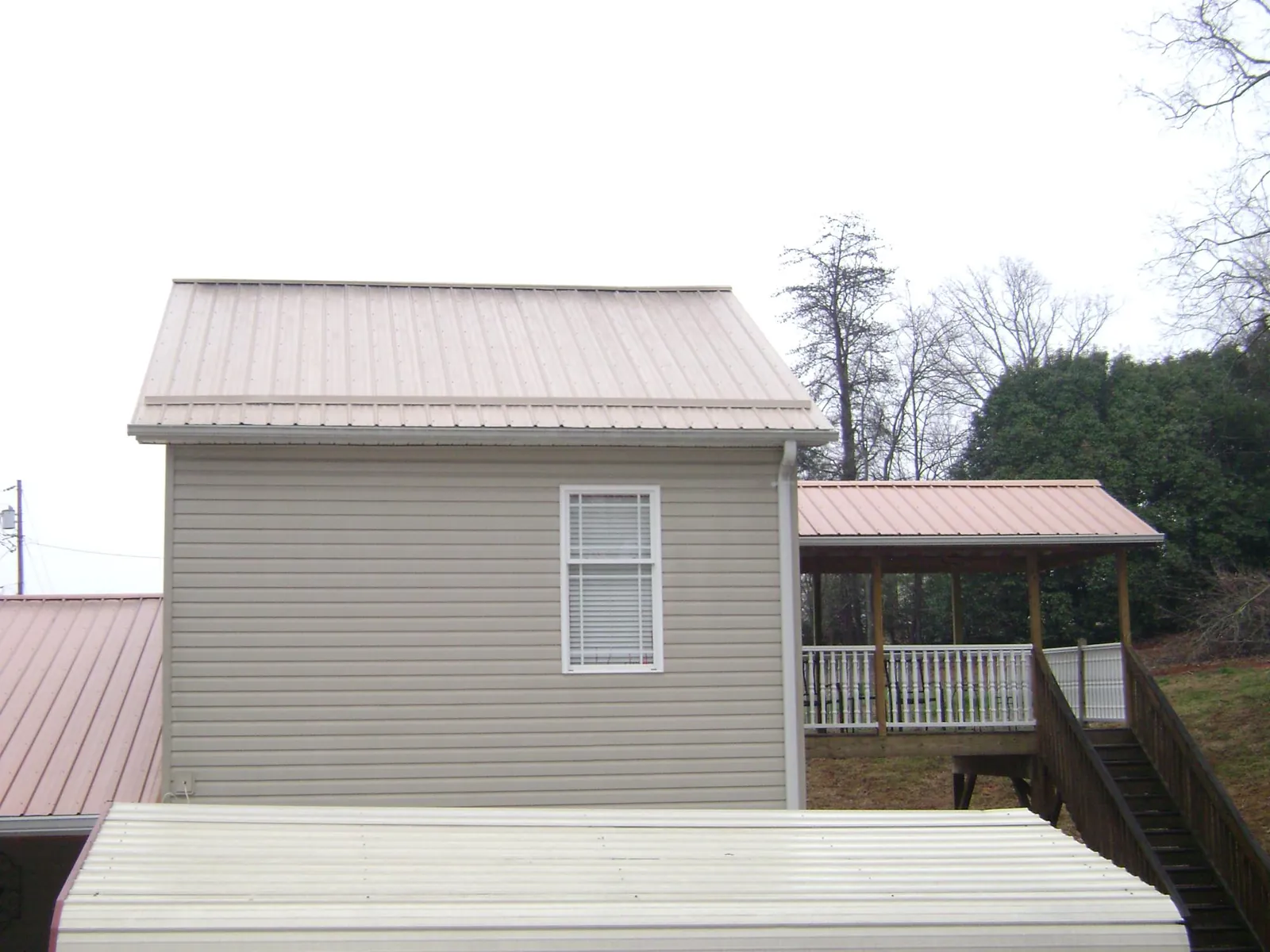 Tan metal roofs on a two story addition and attached porch, from a Roof Replacement job in Mathiston